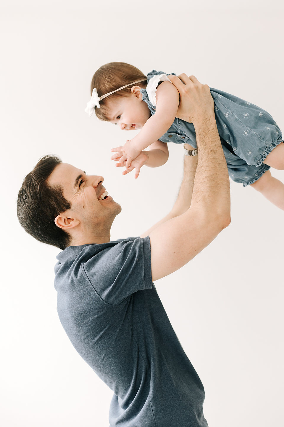 A man lifts a one year old girl into the air