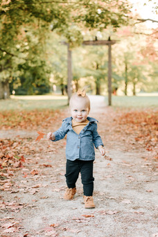 A toddler girl walks on a path under autumn trees