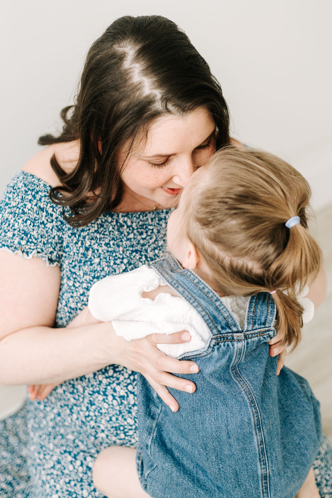 A pregnant woman has a young girl sitting on her lap as they touch nose to nose