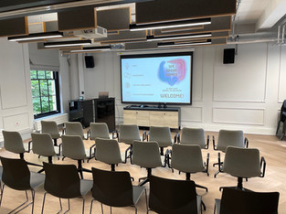 Empty presentation suite set up with chairs and projector displaying We Speak Games welcome slide