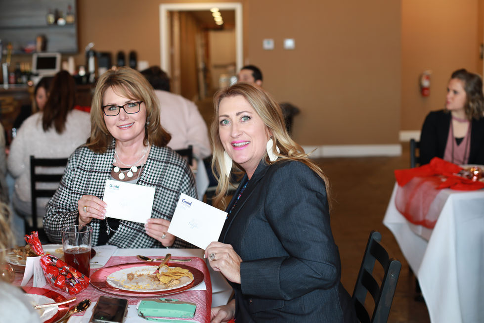 Portrait of two women sitting at a table holding envelopes that say gold