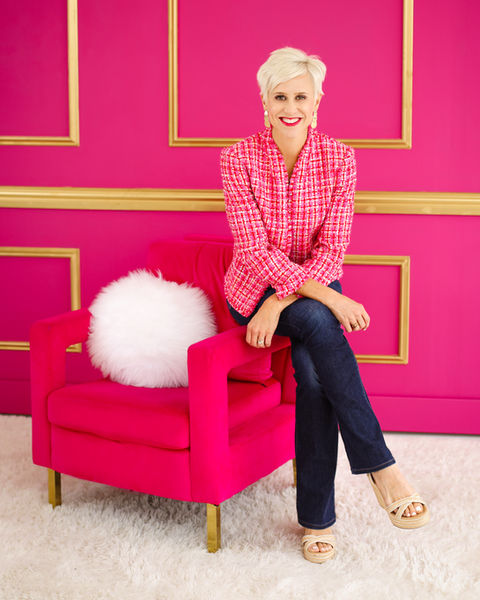 Portrait of a woman sits in a pink chair in front of a pink wall
