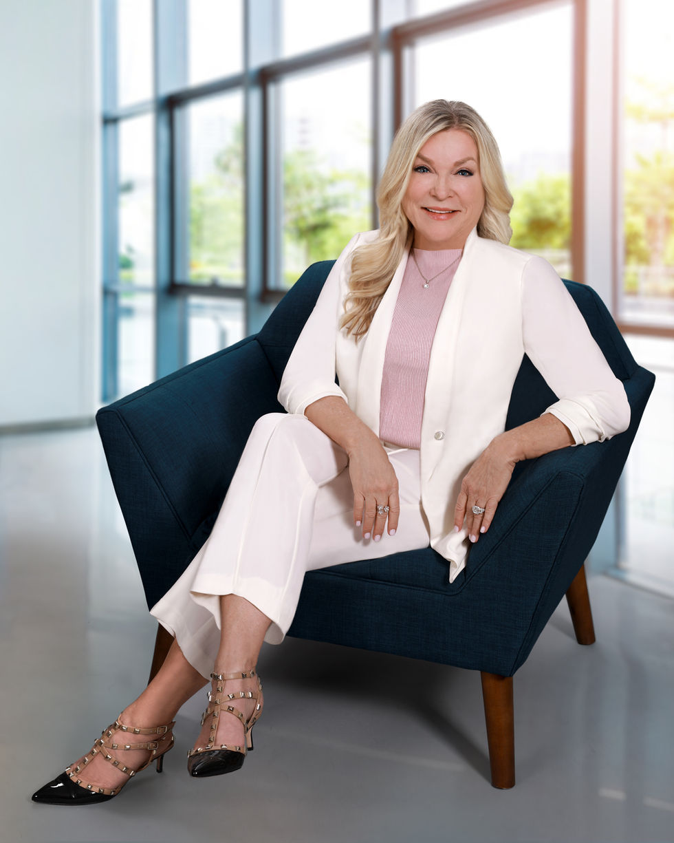 Portrait of a woman in a white suit sits in a blue chair