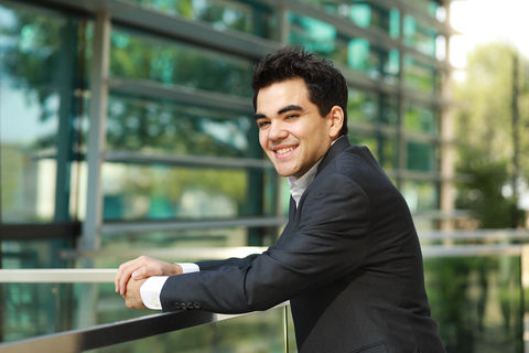 Headshot of a man in a suit leans on a railing and smiles