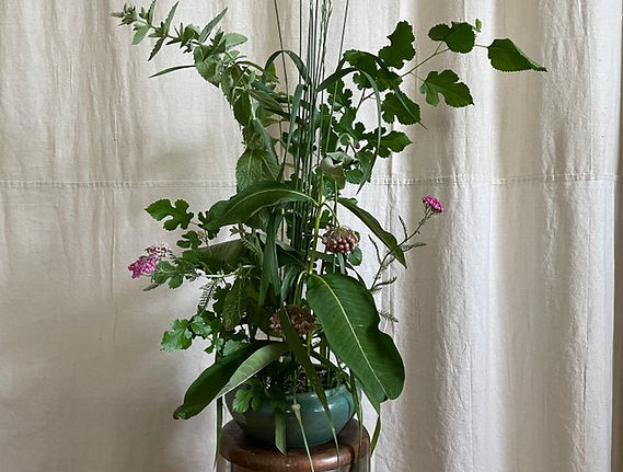 an arrangement of wildflowers and branches in a green vessel
