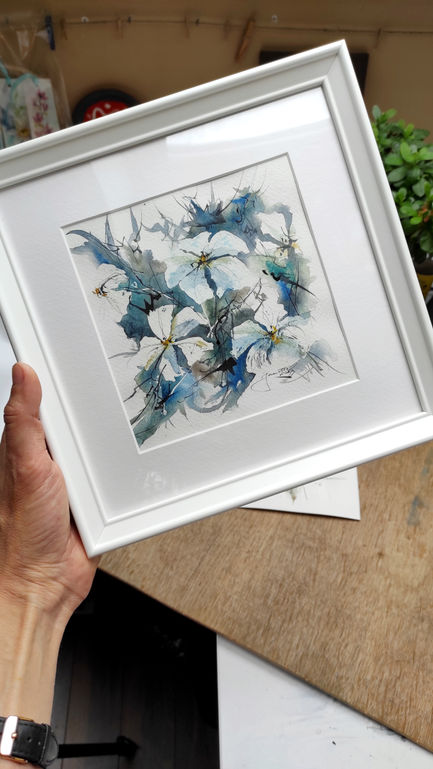 a person is holding a framed painting of blue and white flowers