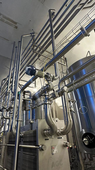 Stainless steel piping and valves beside tanks at a dairy processing facility