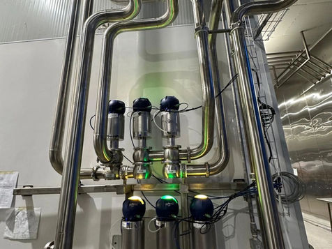 Close view of stainless steel process piping and valve actuators at a dairy processing facility
