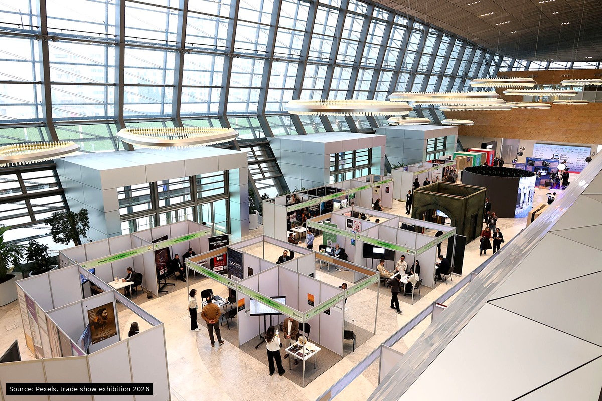 Wide view of delegates meeting across booths in a modern trade-show exhibition hall. Photo source: Pexels.