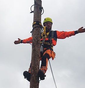 Worker secured with a fall-arrest harness on a utility pole demonstrating safe working practices during overhead line safety and working at heights training.