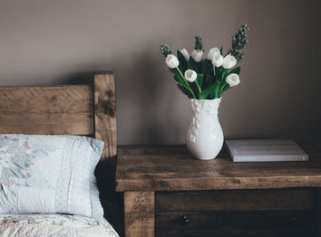Chambre d'un gîte avec un joli pot de fleurs de tulipes blanches posé sur une table de chevet en bois foncé