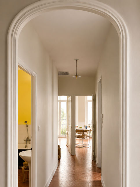 Couloir lumineux avec arche blanche et sol en tomettes.
