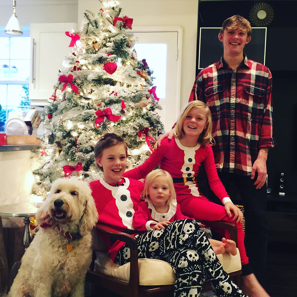Four siblings in red holiday pajamas beside a flocked Christmas tree with the family dog
