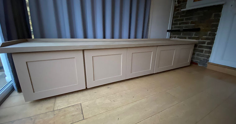 Taupe custom-built window bench with storage in a modern London home, offering both style and practicality