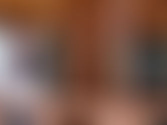 A woman in winter scenery standing on a porch of a log cabin with a cup in her hands, smiling