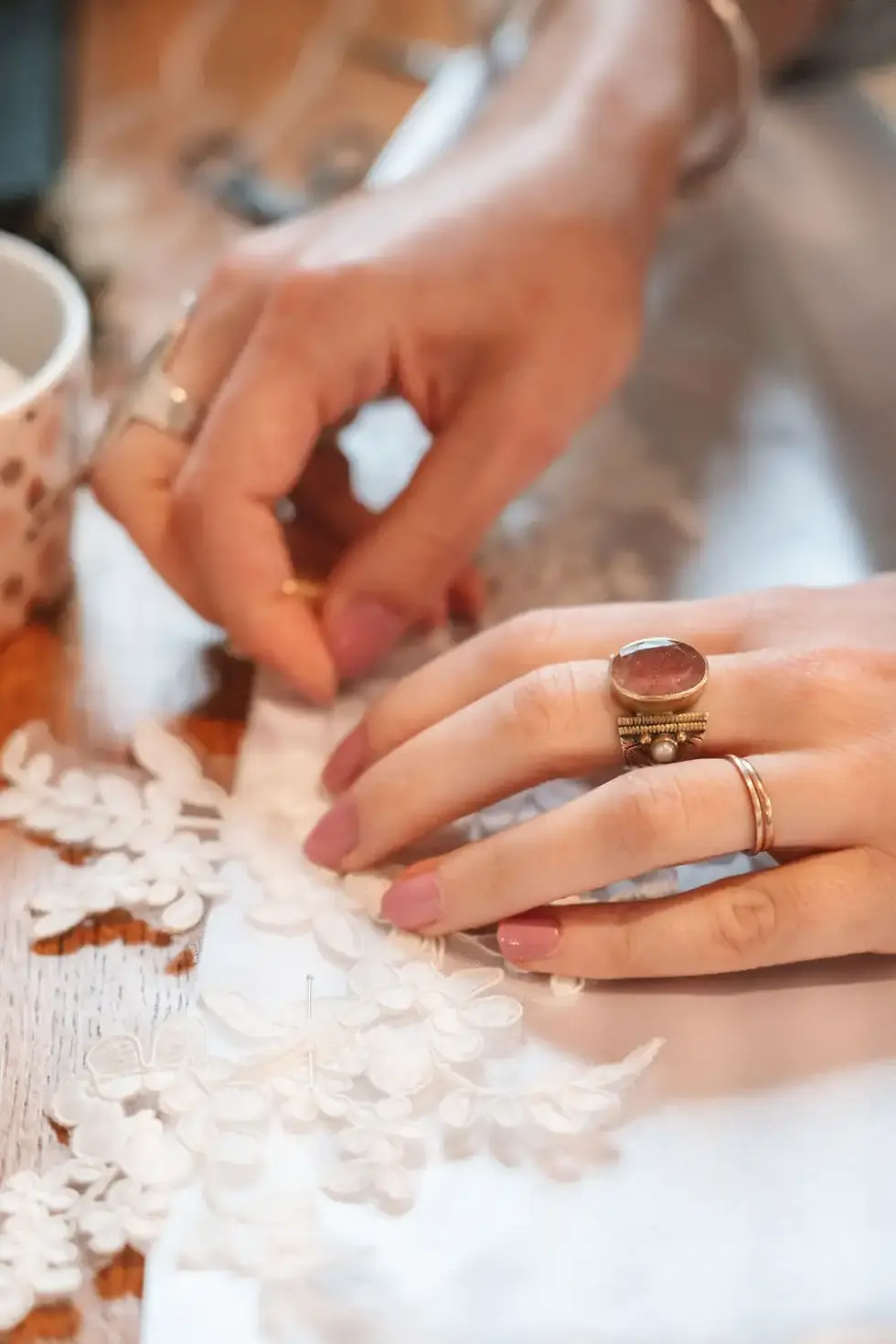 Les mains de Cécile Labrunie en train de coudre de la dentelle sur une robe de mariée