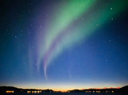 Two streaks of green and red auroras extending to the opposite bank