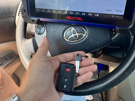 Hand holding a smart key fob in front of a car dashboard during smart key programming
