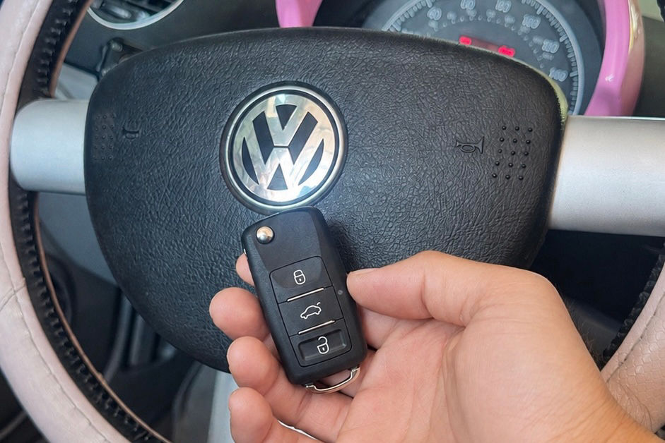 Hand holding a Volkswagen key fob in front of the steering wheel for transponder key programming