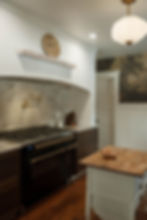 Finished plastered kitchen range hood featuring reclaimed brick surround and wood-tone mural wallpaper accent wall in a historic farmhouse kitchen.