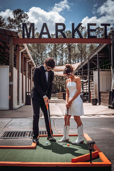 Bride and groom outside, wearing sunglasses, playing mini golf.