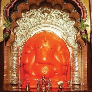 Large orange idol of Lord Ganesha in a decorated temple setting. PANDITJIPUNE