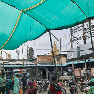 People gather under a green canopy, likely at a market or temple.
