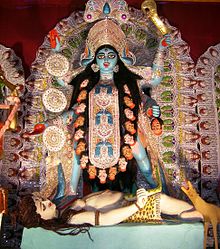 Kali statue holding sword with body, surrounded by elaborate decorations. PANDITJIPUNE