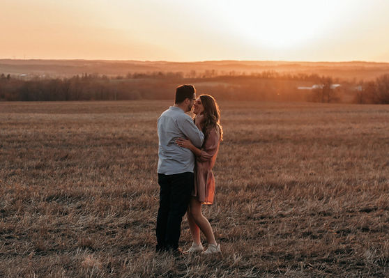 Engaged couple looking at eachother as the sun sets in a field.