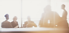 A team of people working together around a table as a sunray casts into the room. 