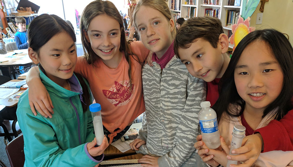 Elementary students at Living Wisdom School in Palo Alto work together during science class, proudly holding water samples for their experiment, demonstrating hands-on, collaborative learning in the classroom.