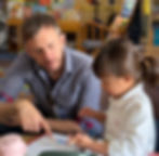 Teacher sitting closely with a young student, guiding them through a learning activity