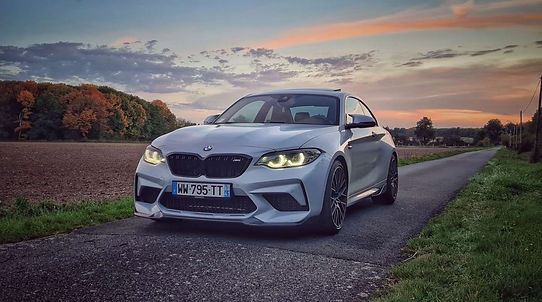 Photographie d'une voiture BMW grise sur une route de campagne au coucher du soleil. 
