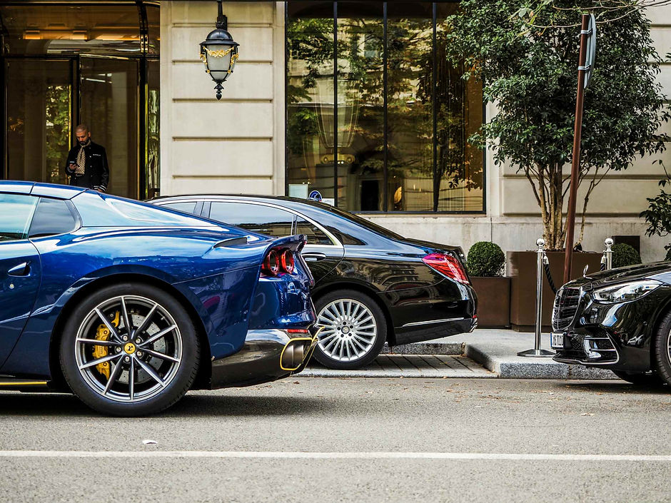A blue sports car and a black chauffeur-style saloon parked outside an elegant Parisian hotel frontage