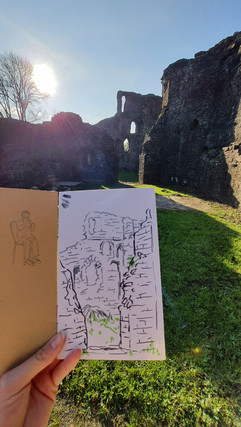 sketchbook page held up in front of a castle ruin
