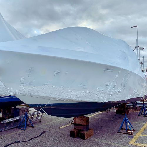 Shrink wrapped motorboat securely covered for winter storage, elevated on blocks and stand