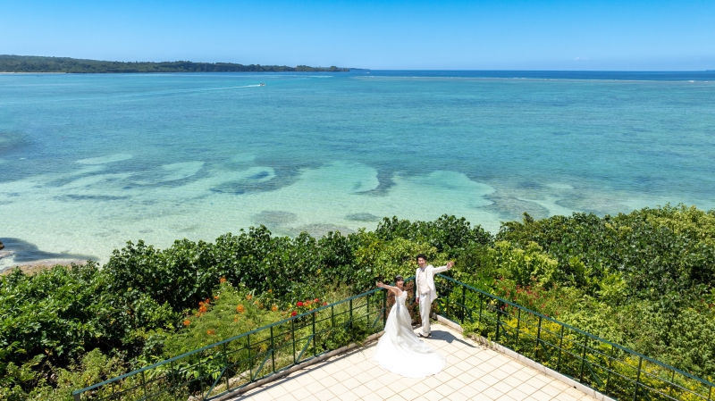 開放的な海を背景に、白いウェディングドレスの女性とタキシードの男性がバルコニーに立ち、腕を広げています。晴天の青空。
場所:沖縄県 恩納村 ムーンビーチ
仕様:海をバックにフォトウエディング