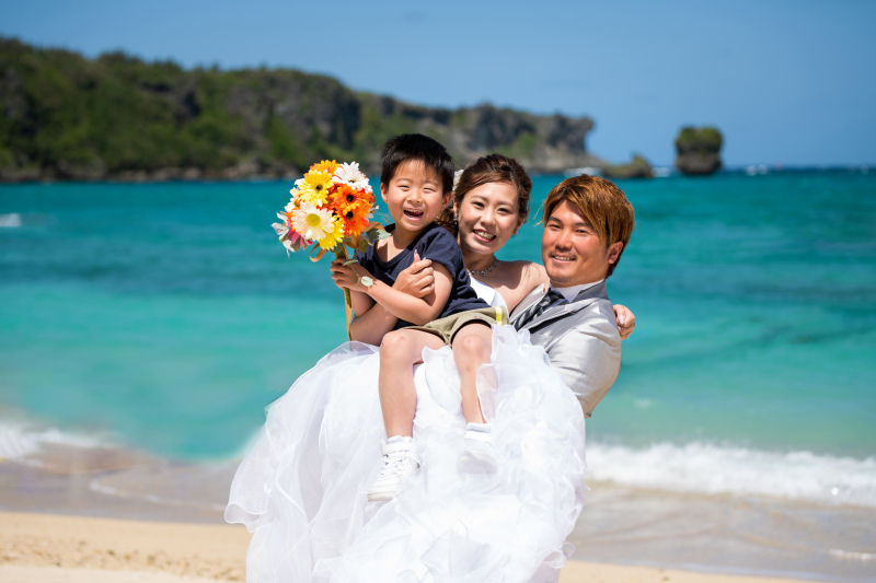 沖縄、恩納村のフォトウェディング。お子様と新婦様を笑顔で抱っこする、ファミリービーチフォトの様子。