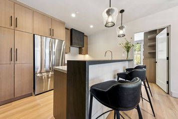 View of the kitchen island with dark base cabinetry, a bright countertop, and bar seating with black leather stools.