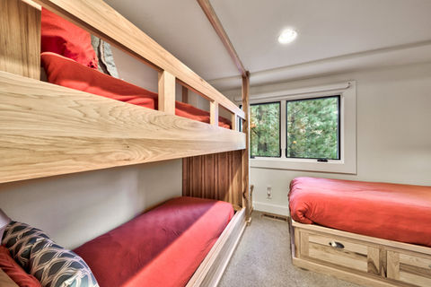 A functional and fun custom bedroom featuring solid wood built-in bunk beds and a matching lower bed with integrated drawers, designed to maximize sleeping capacity for guests.