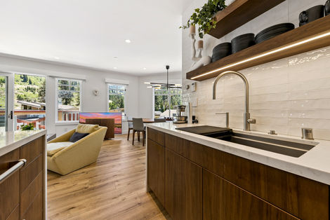 Detail of the sink area, showing the single-bowl undermount sink, white subway tile backsplash, and floating wood shelves with integrated lighting.