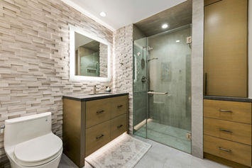 Modern bathroom featuring a floating wood vanity, an illuminated mirror, and a wall clad in textured horizontal stacked stone.