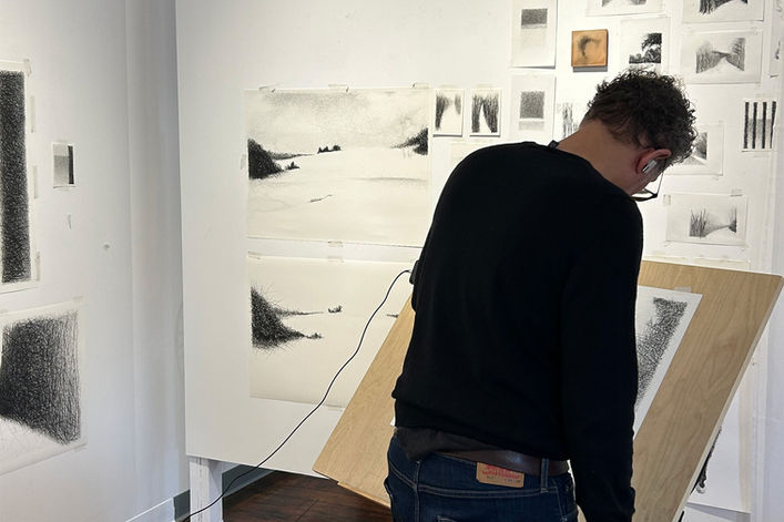 artist Douglas Gilbert standing in front of his drafting table in his studio. Many drawings on the wall.