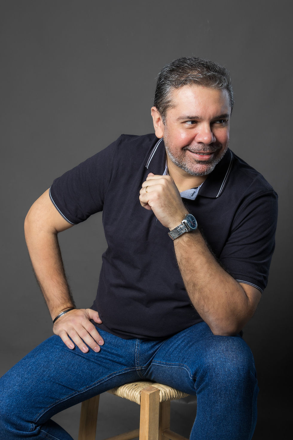 Retrato profissional de consultor de negócios sentado em banco de madeira, fundo cinza neutro, foco no rosto sorridente