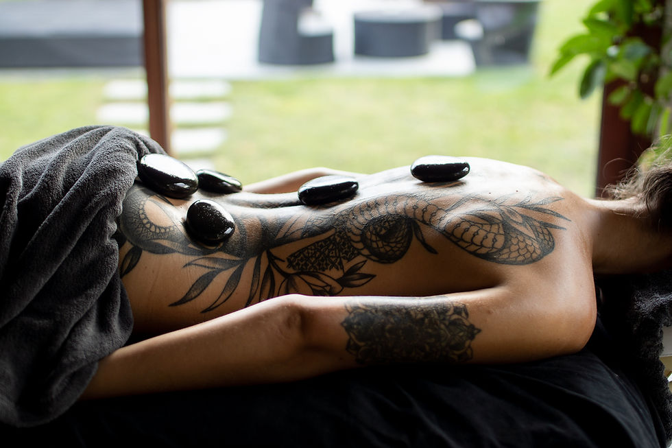 Femme tatouée allongée sur le dos recevant un massage aux pierres chaudes.