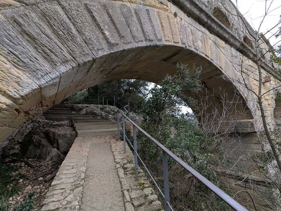 An arch on a stone aqueduct bridge going over a stone path with an iron railing next to it.