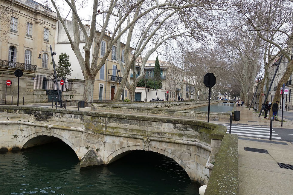 An urban canal with a small, arched bridge spanning it in the foreground.