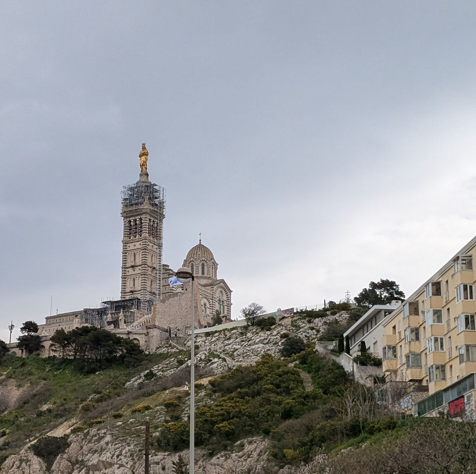 Notre Dame de la Garde from the neighborhood directly below the hill. An apartment building is to the right and the church is on top of the hill.