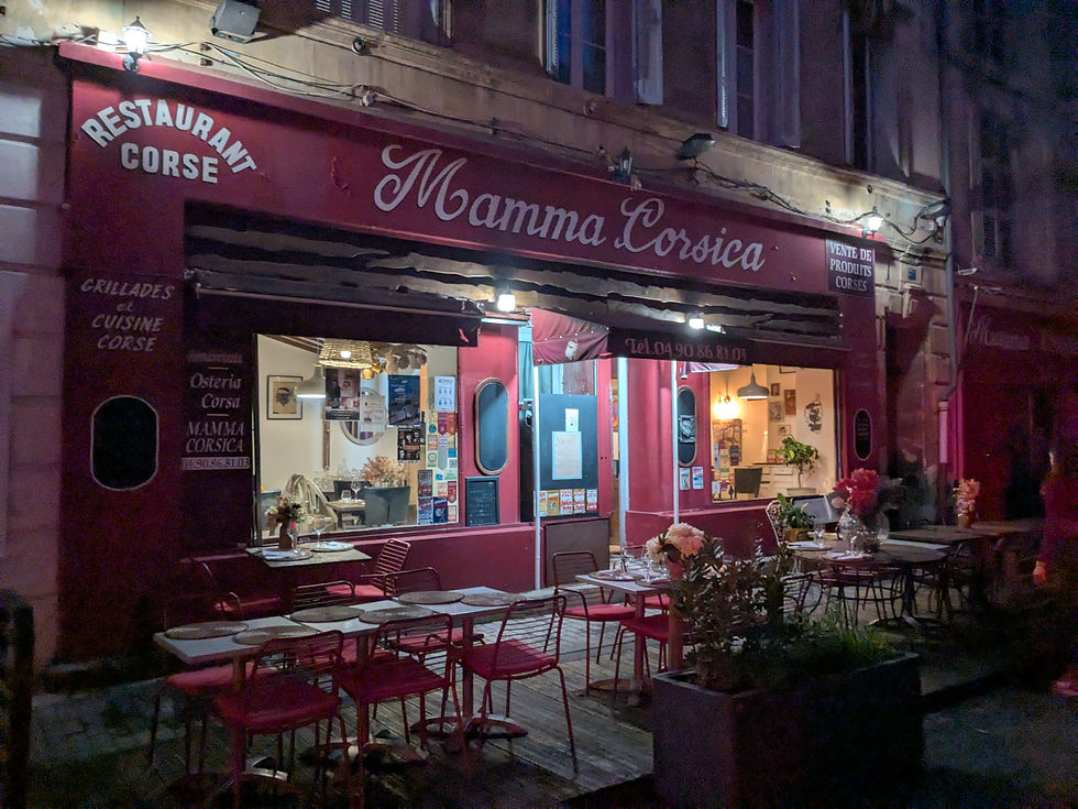 The exterior of the restaurant Mamma Corsica. The facade is red and there are many tables and chairs outside. It's night.