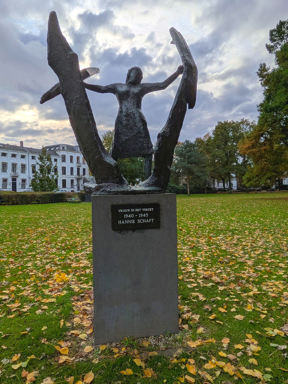 A bronze statue on a large, rectangular plinth. The statue depicts a woman breaking free from a barrier keeping her restrained. The plaque on the plinth reads, "Vrouw in Het Verzet. 1940-1945. Hannie Schaft."